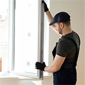 Man in dark overalls and dark baseball cap installs a window 