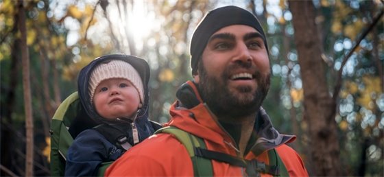 Smiling man exploring the woods with a baby on his back.