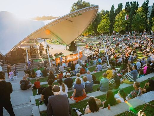 Crowd sitting at an outdoor amphitheatre listening to a band with the sun setting in the background