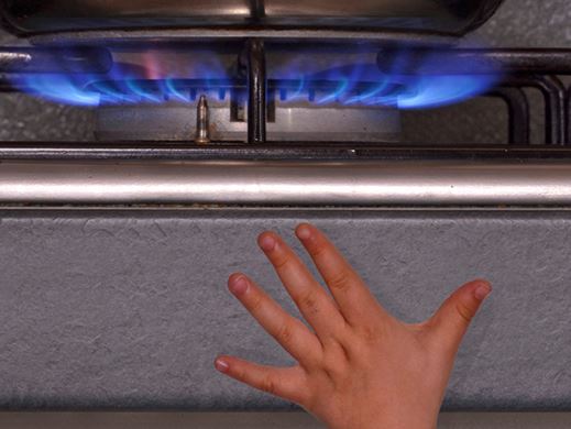 A small child&#39s hand reaches up from the edge of the image towards a gas stove flame.