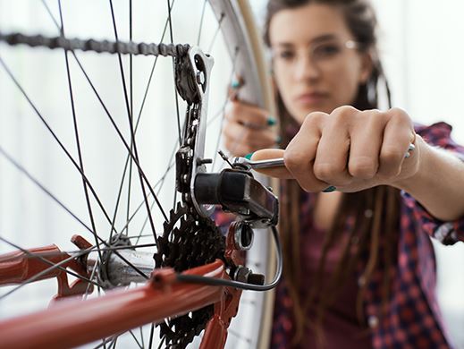 A woman wearing glasses and a red flannel shirt is repairing the wheel of a bike