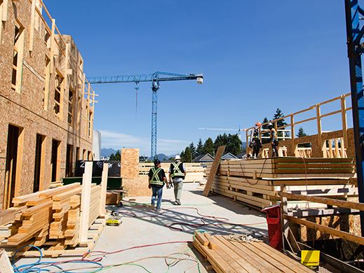 An image of the backs of two men wearing high-vis vests and safety attire on a construction site.