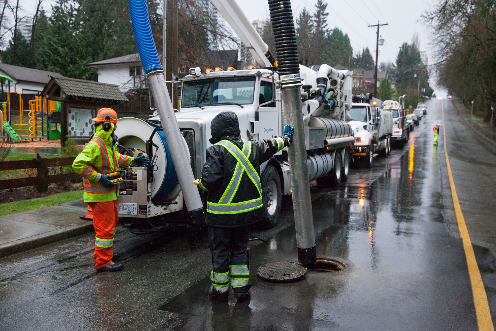 Two Public Works crew members wearing high-vis vests work with a vacuum truck.