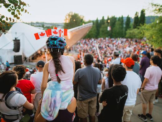 Young girl with mini Canada flags on her bike helmet watching Canada Day performances at the Plaza