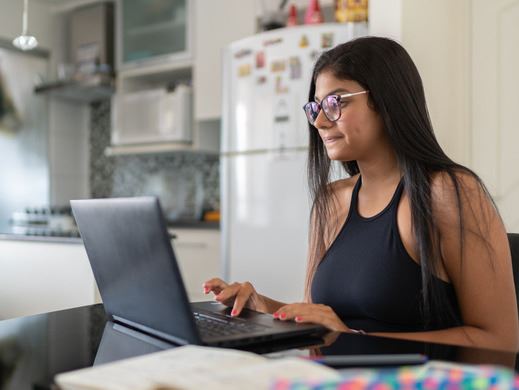 Picture of a woman sitting at table in her kitchen with a laptop open in front of her