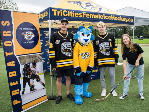 A group of Tri-City Female Ice Hockey players standing in front of a tent on a turf field.