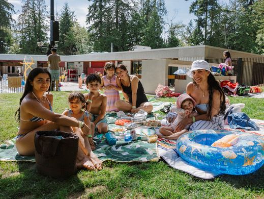 A young family sitting on the Mundy Park Pool lawn enjoying a picnic on a sunny day.