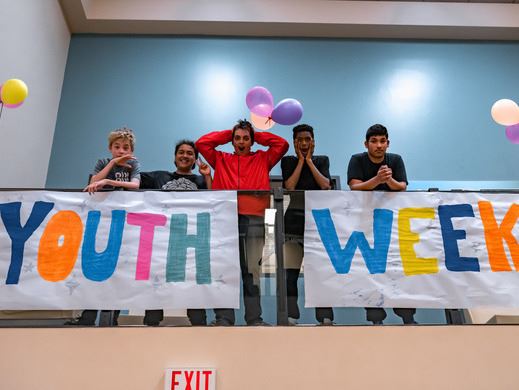 Youths standing behind a railing with a Youth Week banner visible in front