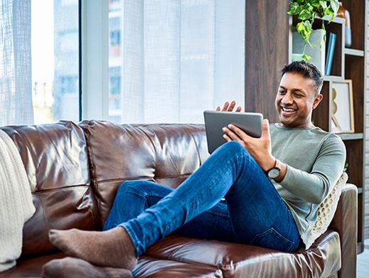 Man sitting on a couch and scrolling on a tablet.