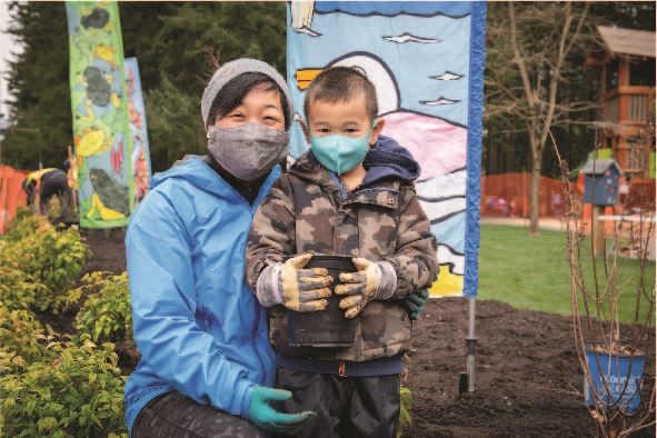 Adult and child pose with plant during volunteer planting event
