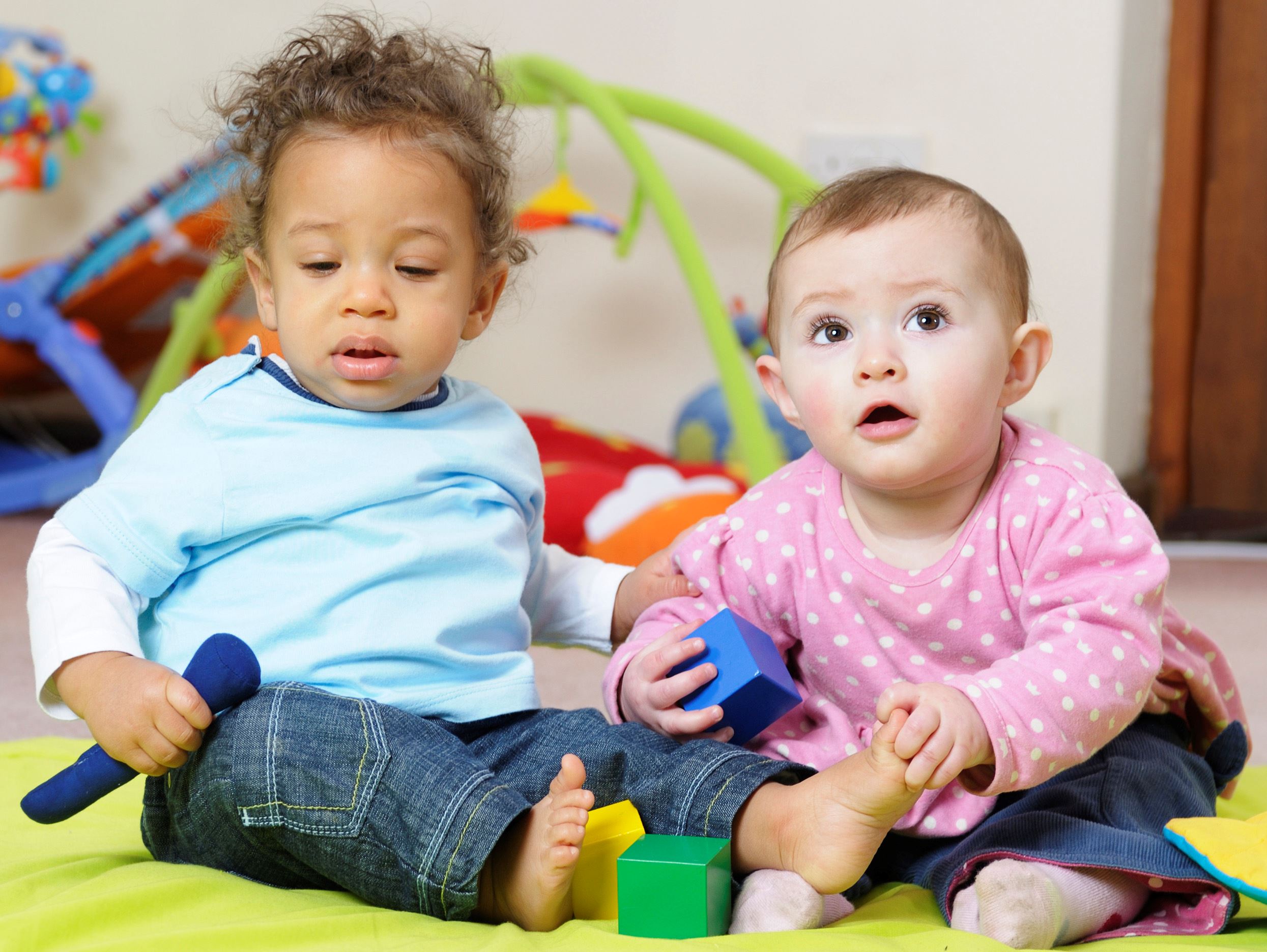 Two babies sit on the floor playing with blocks