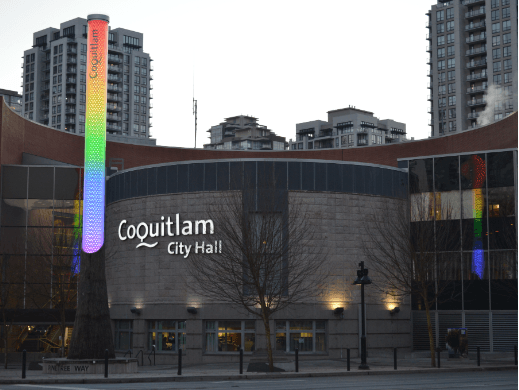 Photo of the exterior of Coquitlam City Hall at dusk with the light Column lit up in rainbow colours