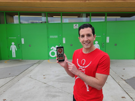 A person holding a cell phone with the GoHere app open while standing infront of washrooms