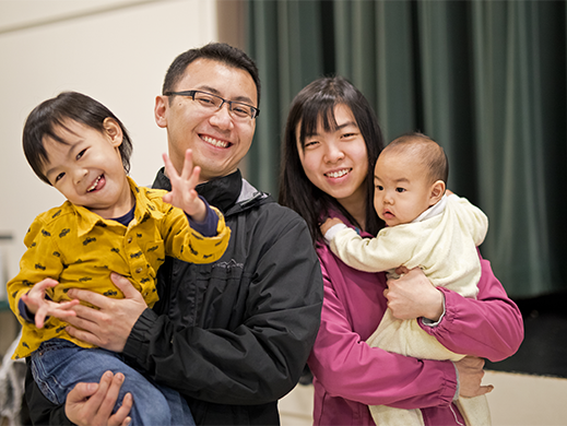 A man holding a toddler and a women holding a baby