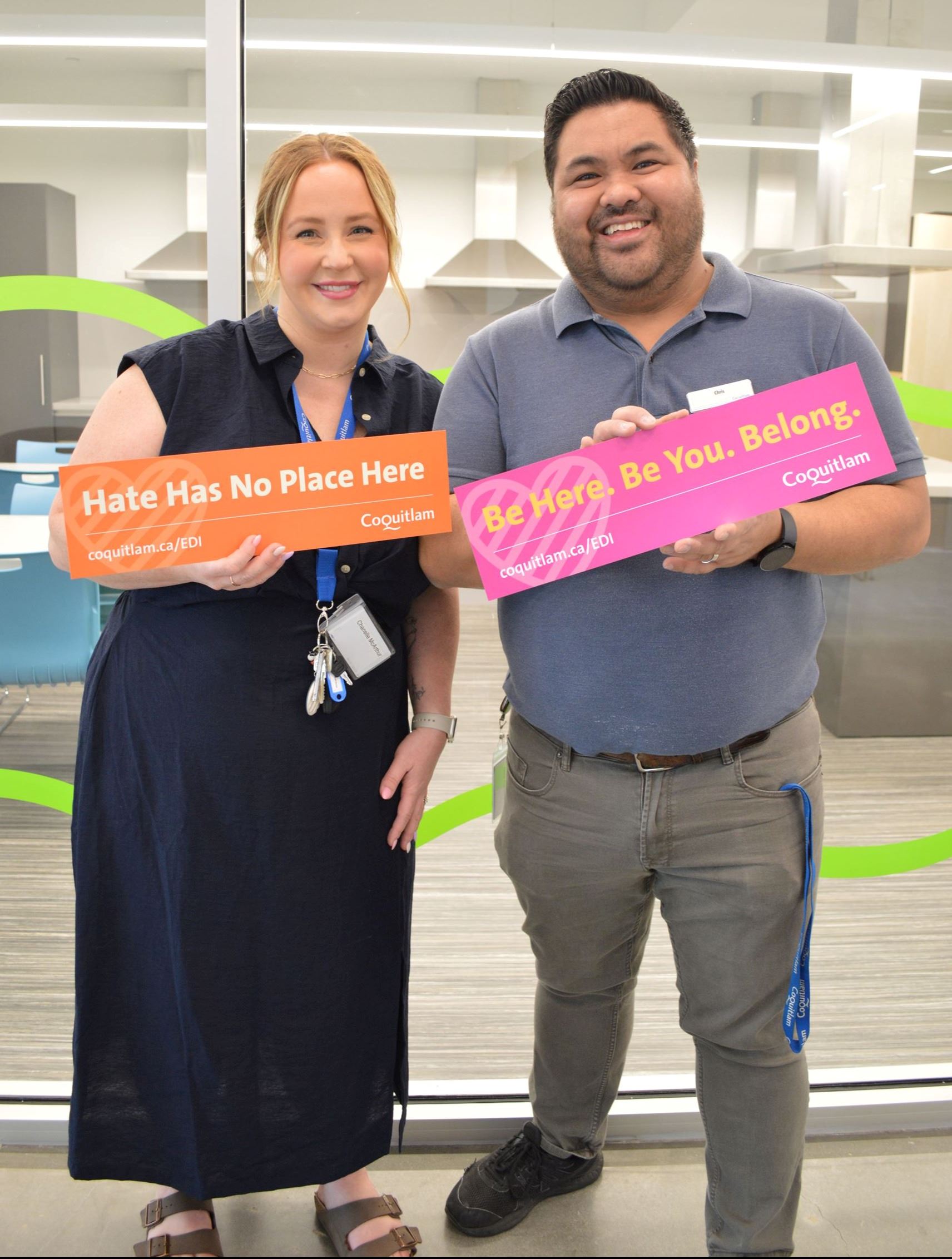 Man and woman standing, smiling, while holding diversity statement signs.