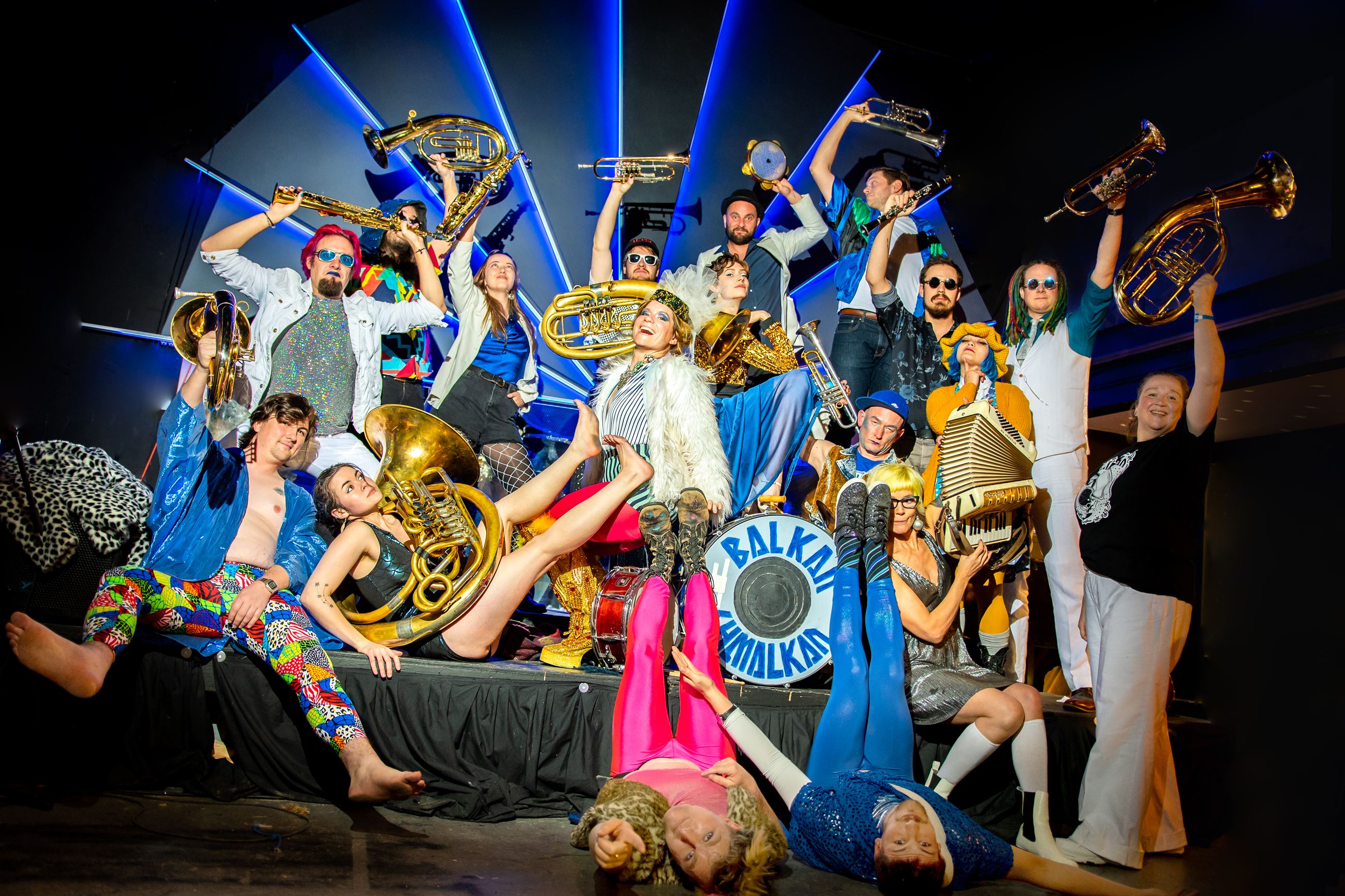 All 18 band members dressed in bright colours holding brass instruments in a fun energetic pose