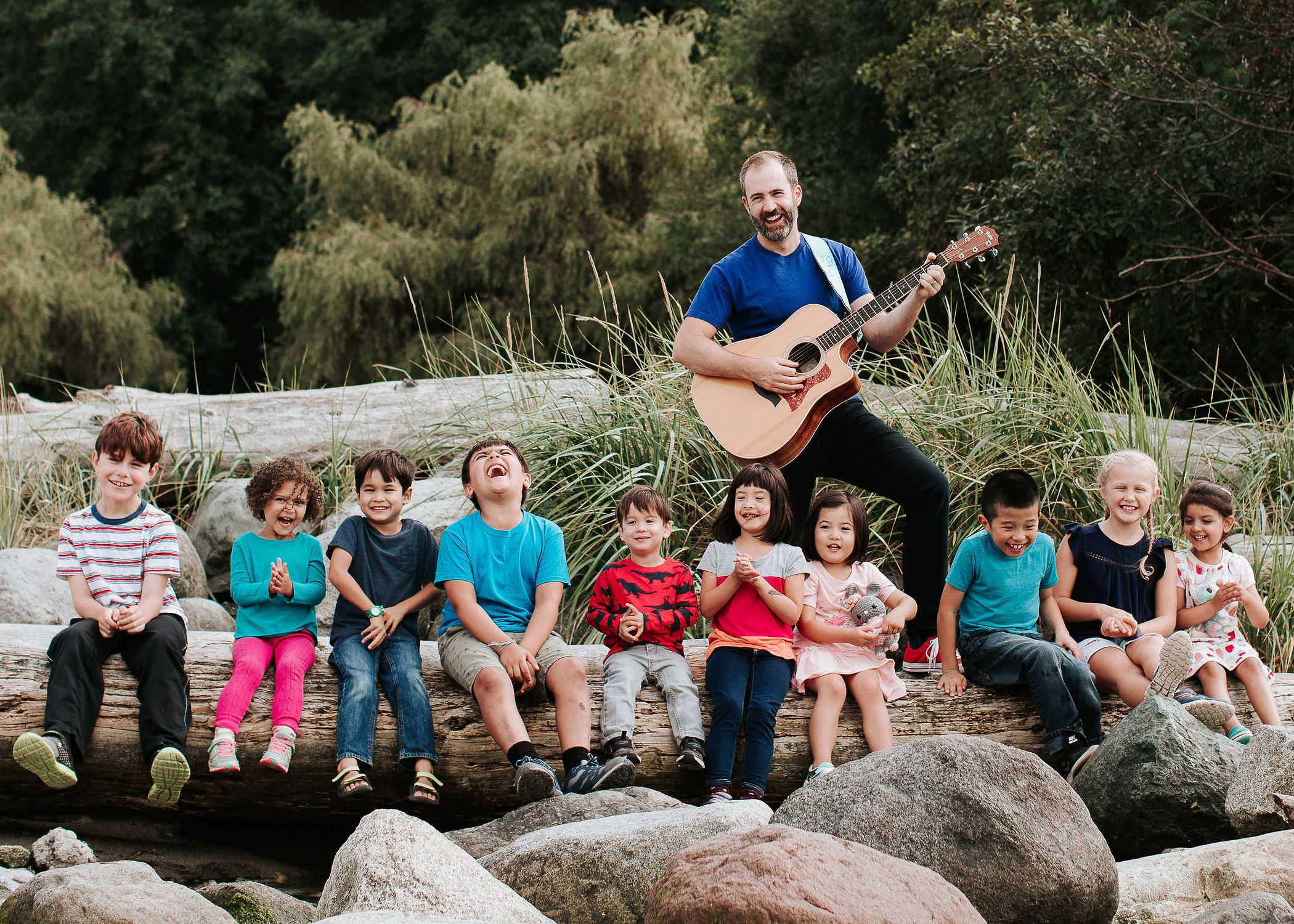 Will standing along a river holding his guitar and a dozen young children sitting in front of him