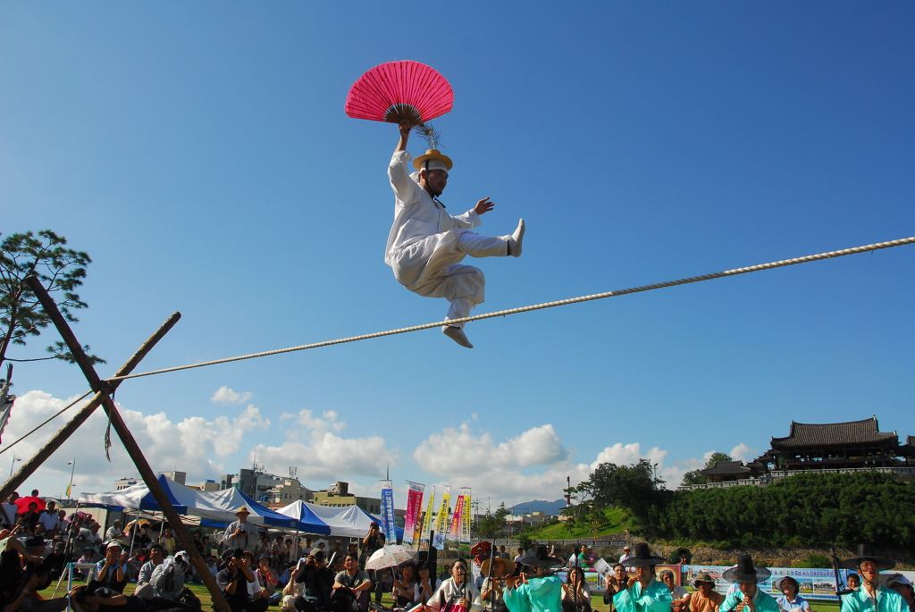 Tightrope walker holding a red fan jumping on a tightrope 10 feet in the air above a crowd